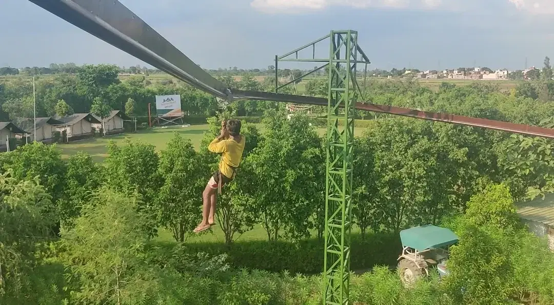 Zipline rider passing over greenery at Great Rocksport, Sonipat