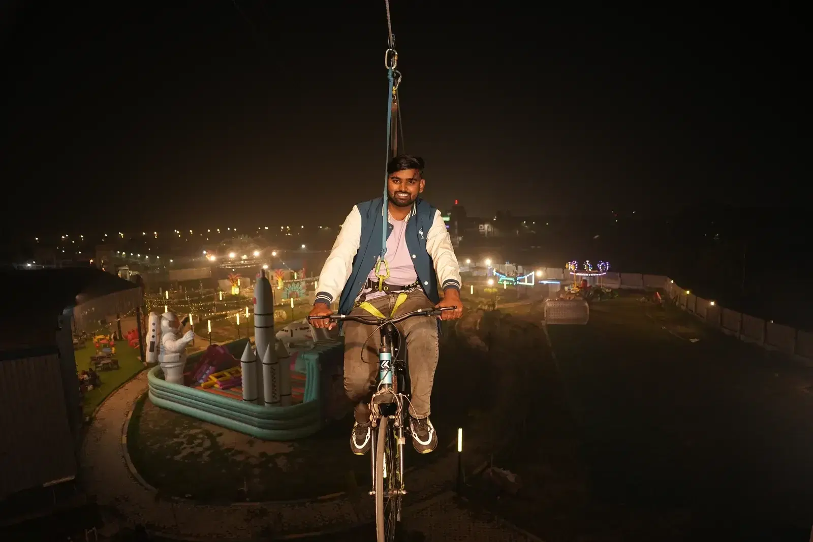 Sky cycle rider crossing above the illuminated JSR Park at night